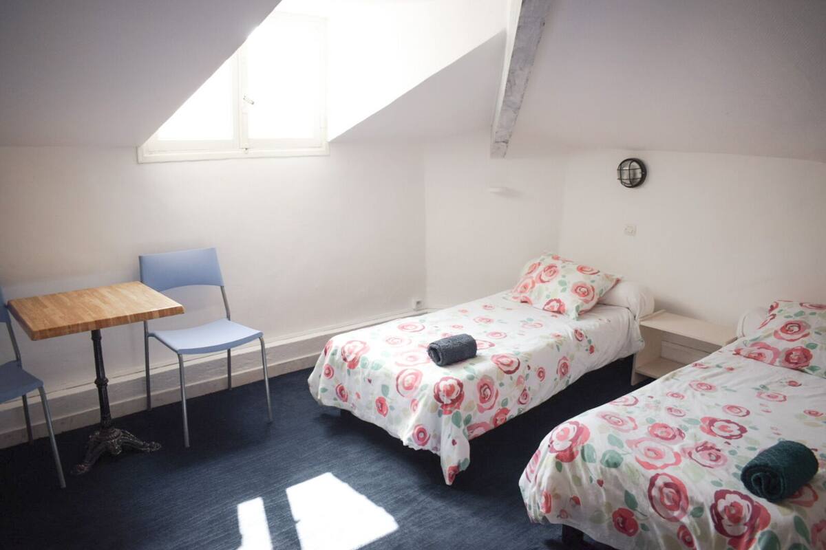 Un dormitorio con una cama individual, una silla, una mesita y un tragaluz.