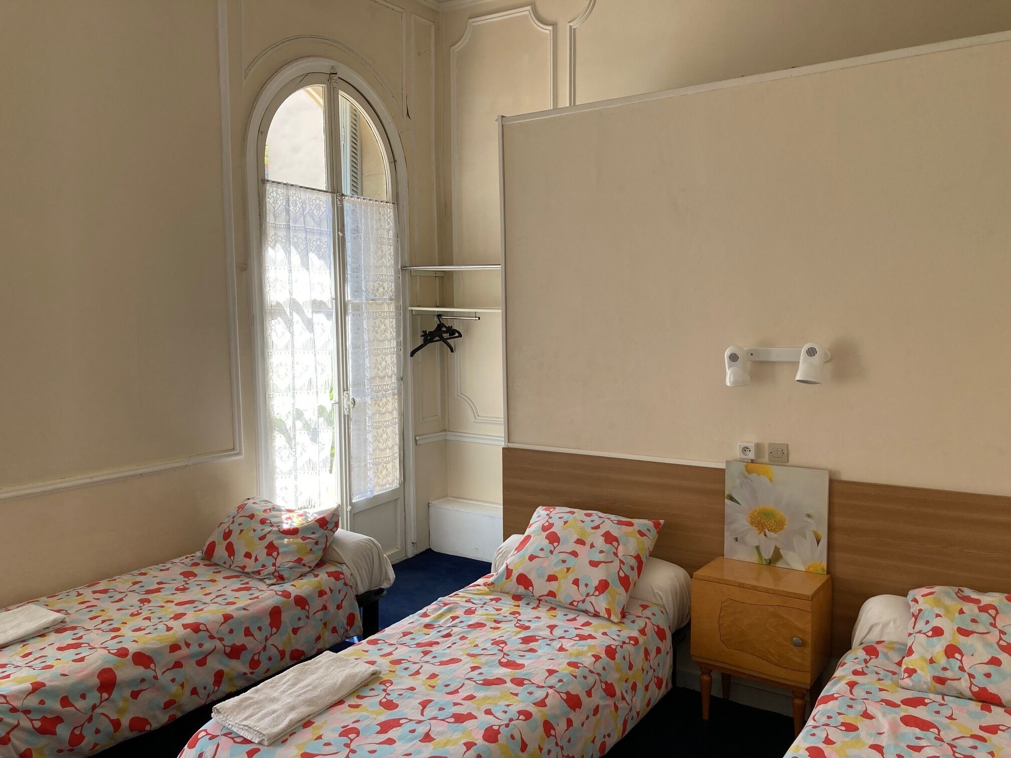 A hotel room with two single beds, a wooden nightstand, a mirror, and a window with a decorative curtain.