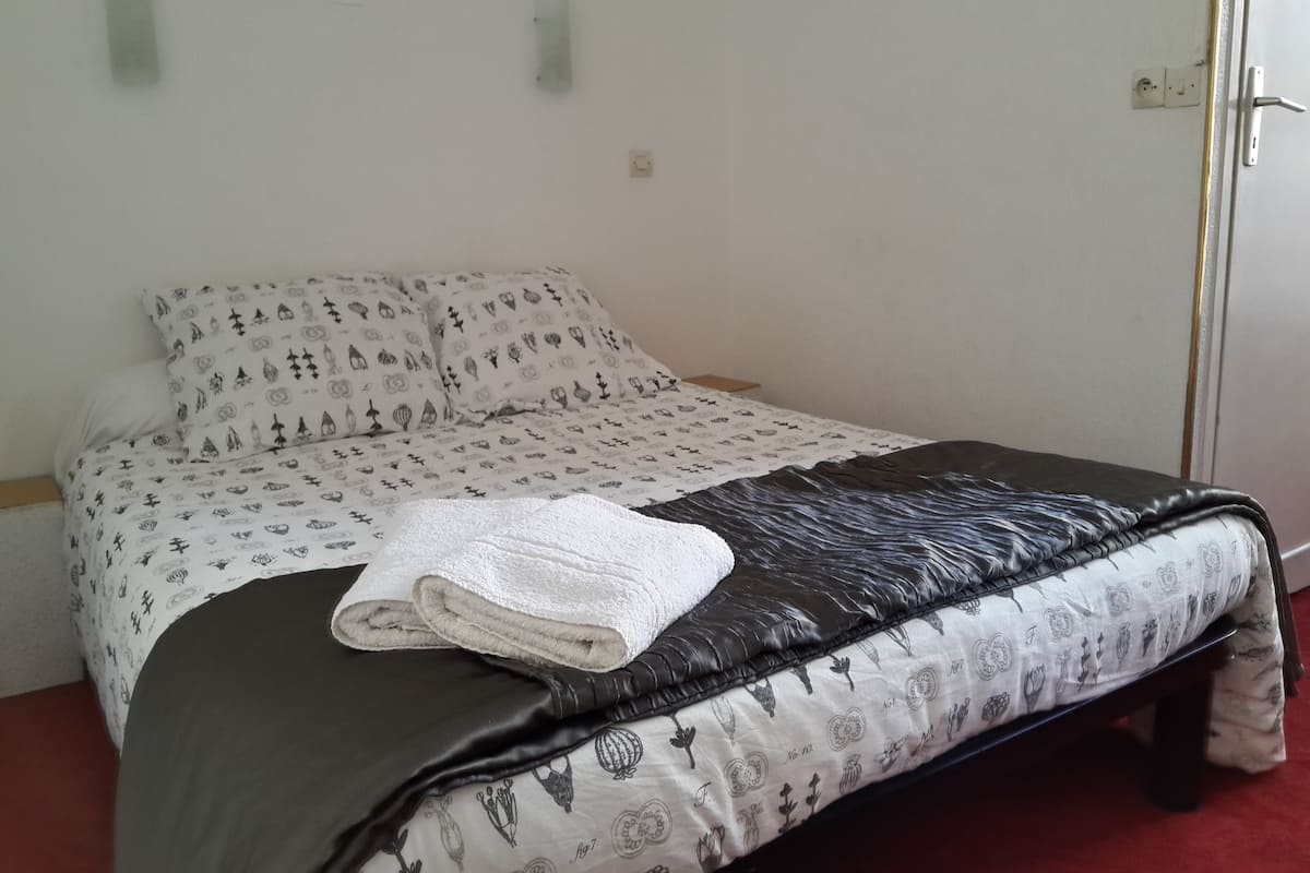 Una cama con ropa de cama estampada, una toalla blanca doblada y un edredón negro.