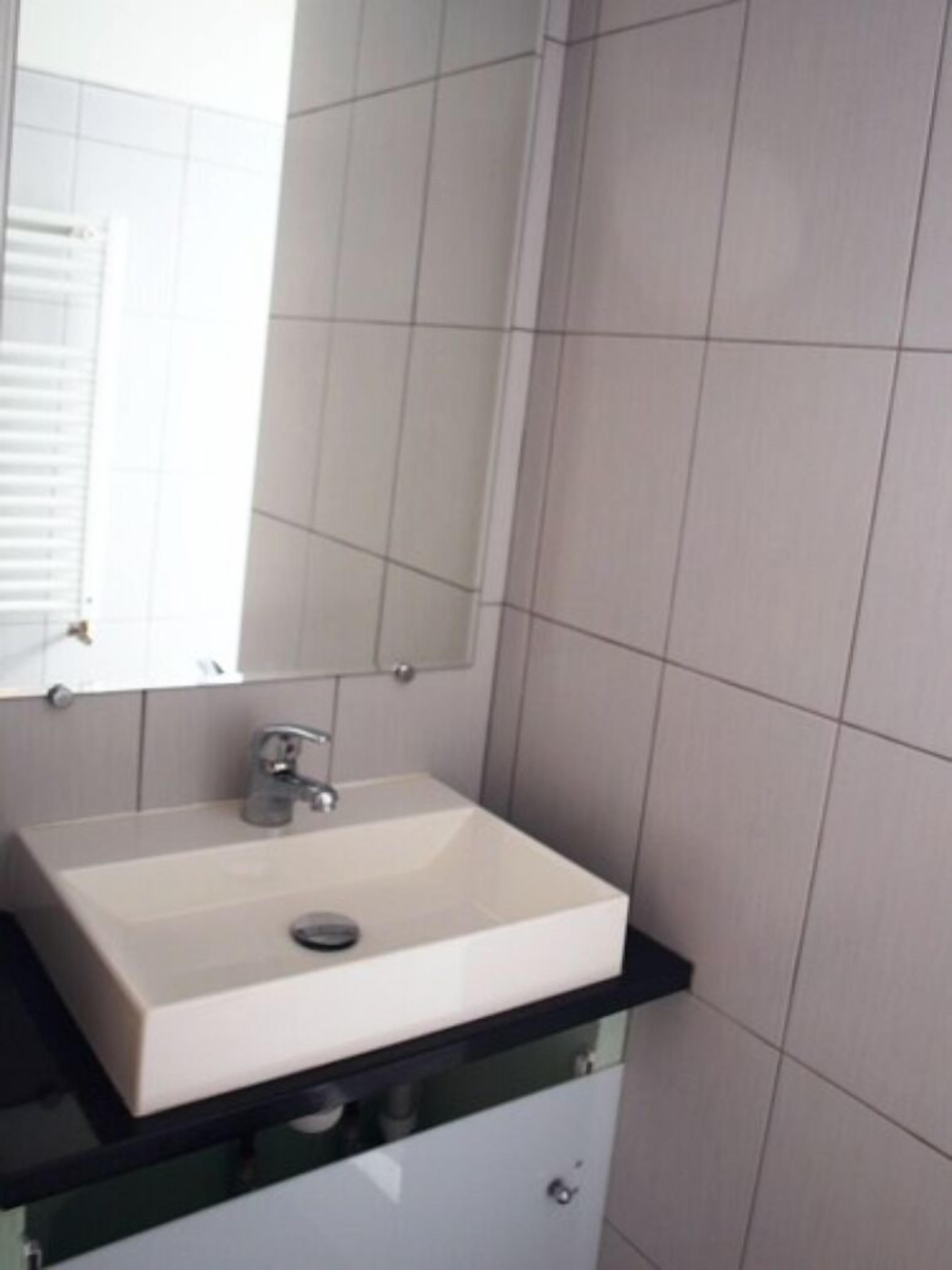 A bathroom with a white sink, a mirror, and tiled walls.