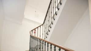 A staircase with marble steps and a wooden handrail, leading to a landing with a white wall and a black metal railing. - Hôtel Belle Meunière (Nice)