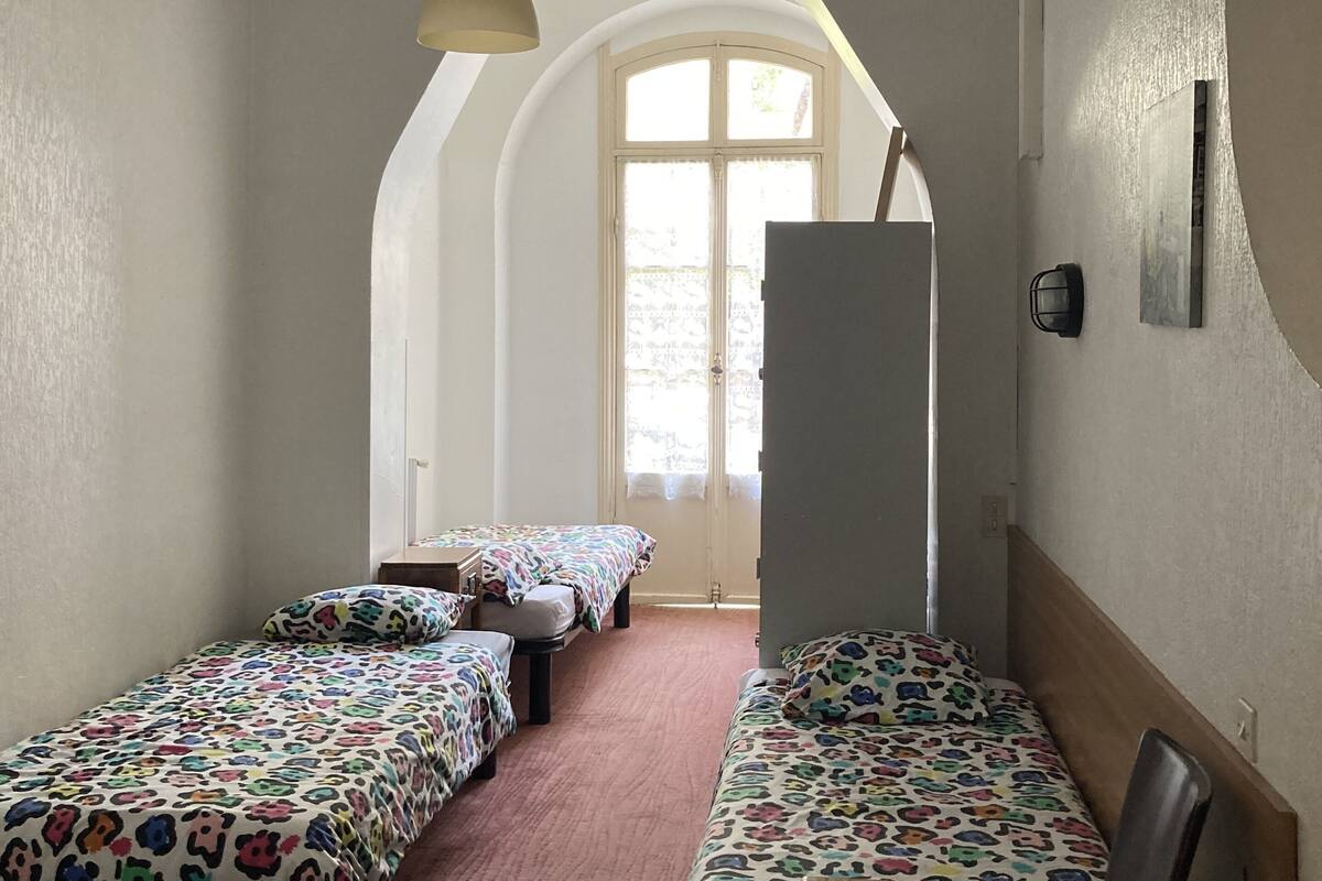 Un dormitorio con dos camas individuales, una mesa de madera y un amplio ventanal de arco.