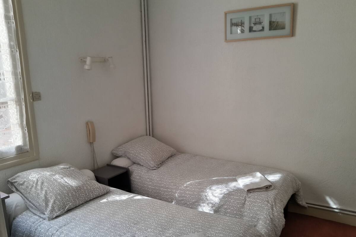 Una habitación pequeña y limpia con dos camas, una mesita de noche, un teléfono y un cuadro enmarcado en la pared.