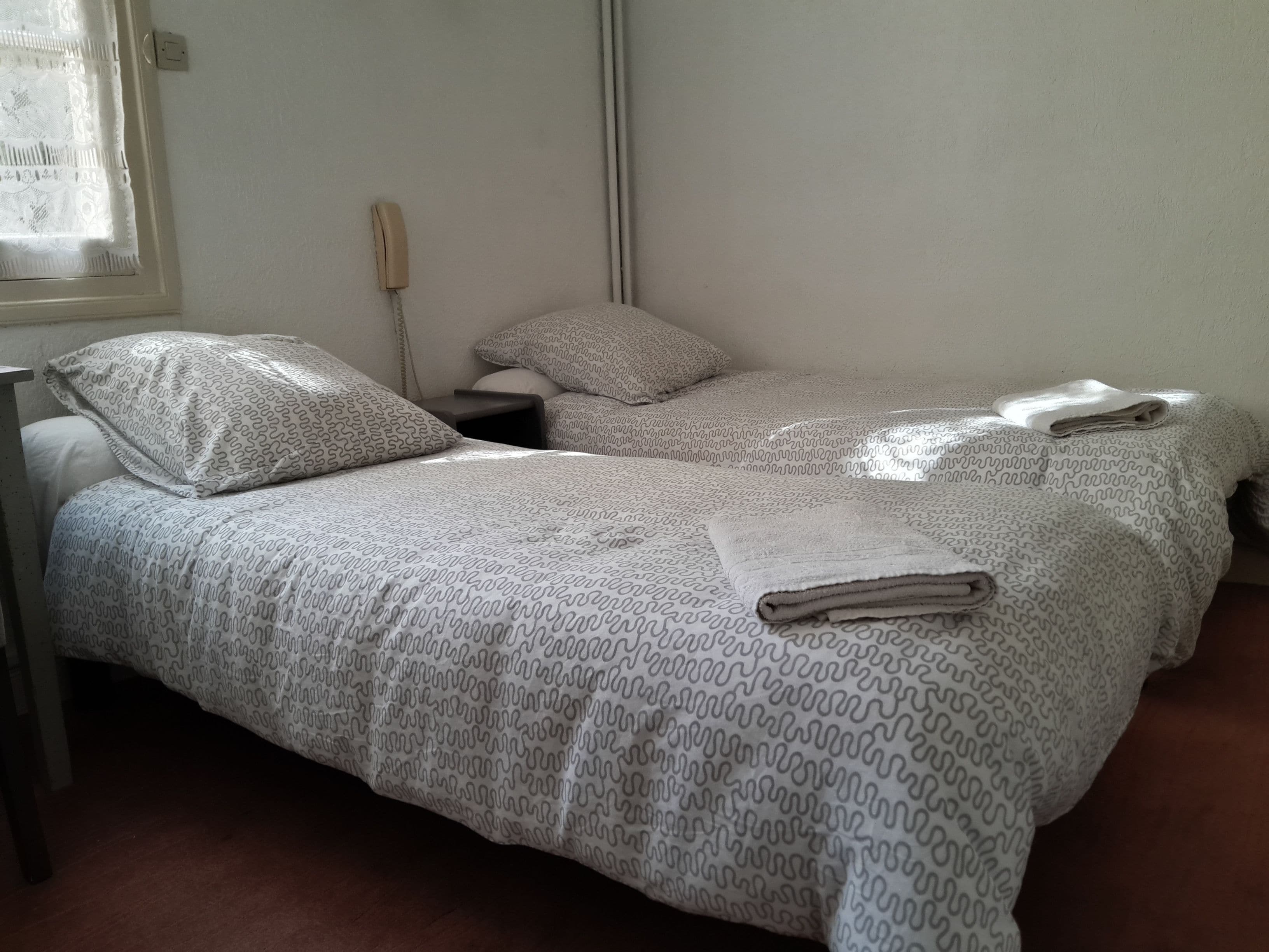 Habitación con dos camas, cada una con ropa de cama y almohadas estampadas, una mesita de noche y un teléfono.