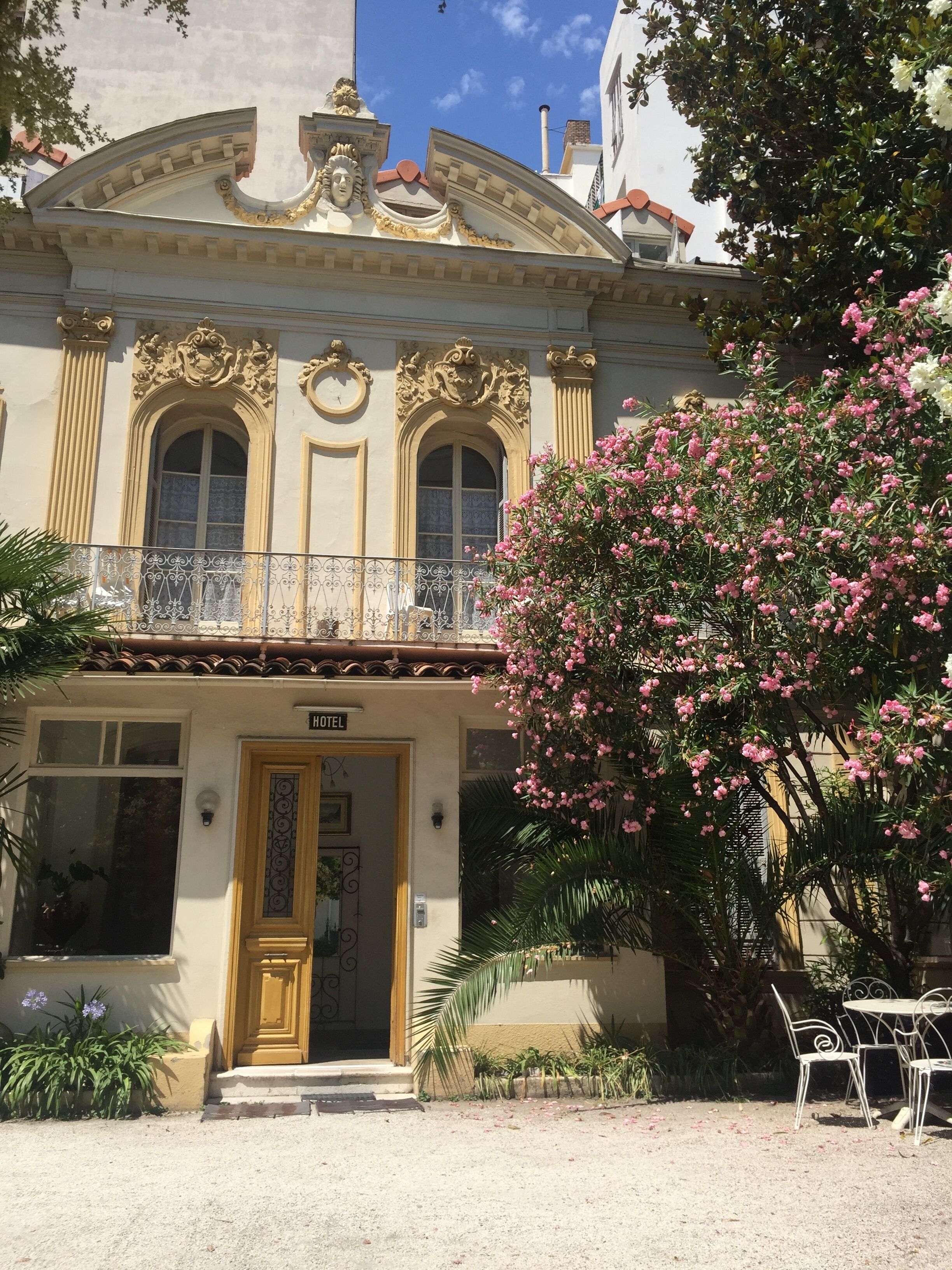 A hotel with ornate architectural details, a balcony, and a large flowering tree in front.