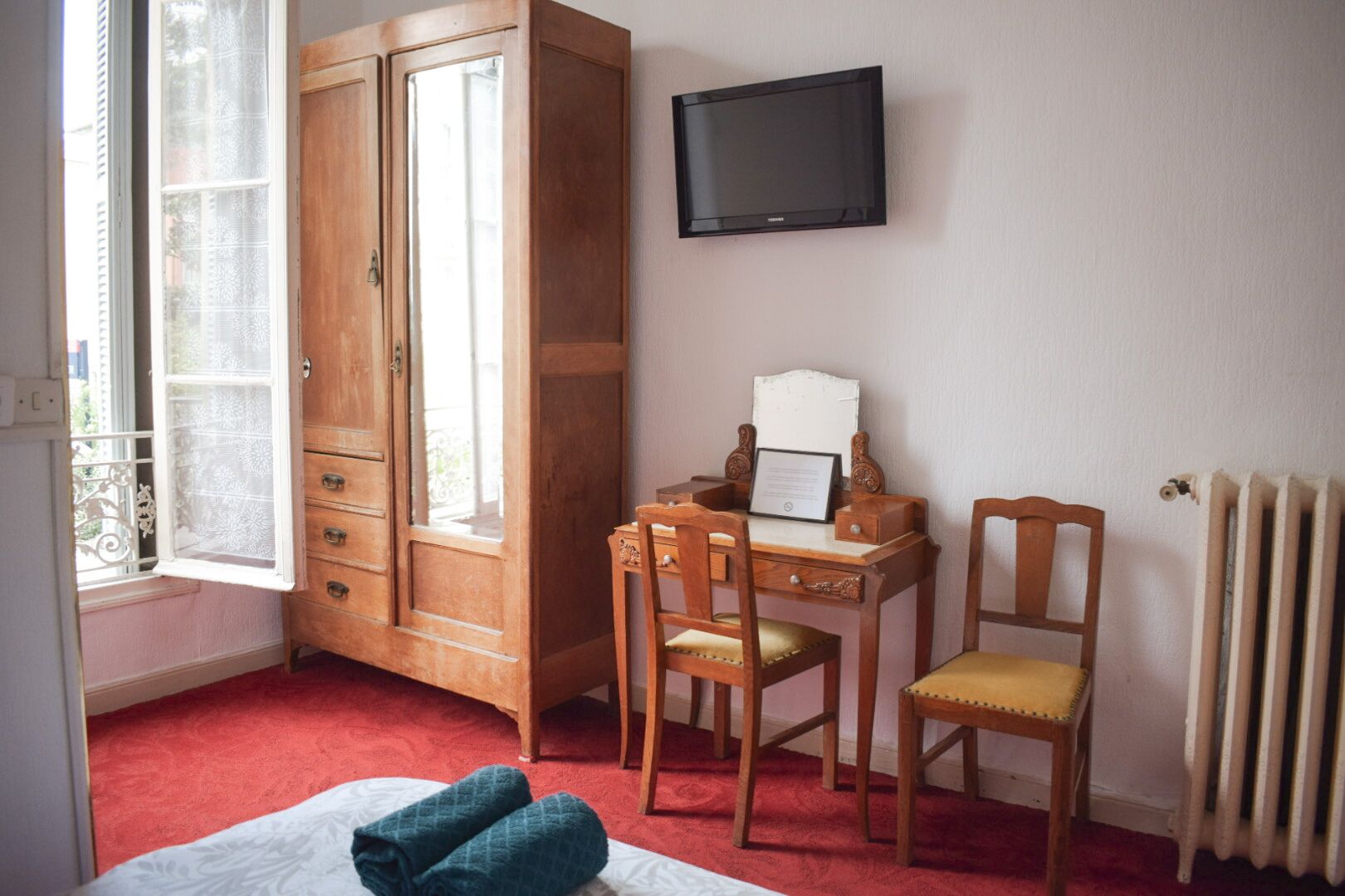 Ein Schlafzimmer mit Holzschrank, Schreibtisch mit Stuhl, Bett und Fernseher an der Wand.