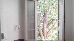 A room with a bed, a desk, a chair, and a window with a tree view. - Hôtel Belle Meunière (Nice)