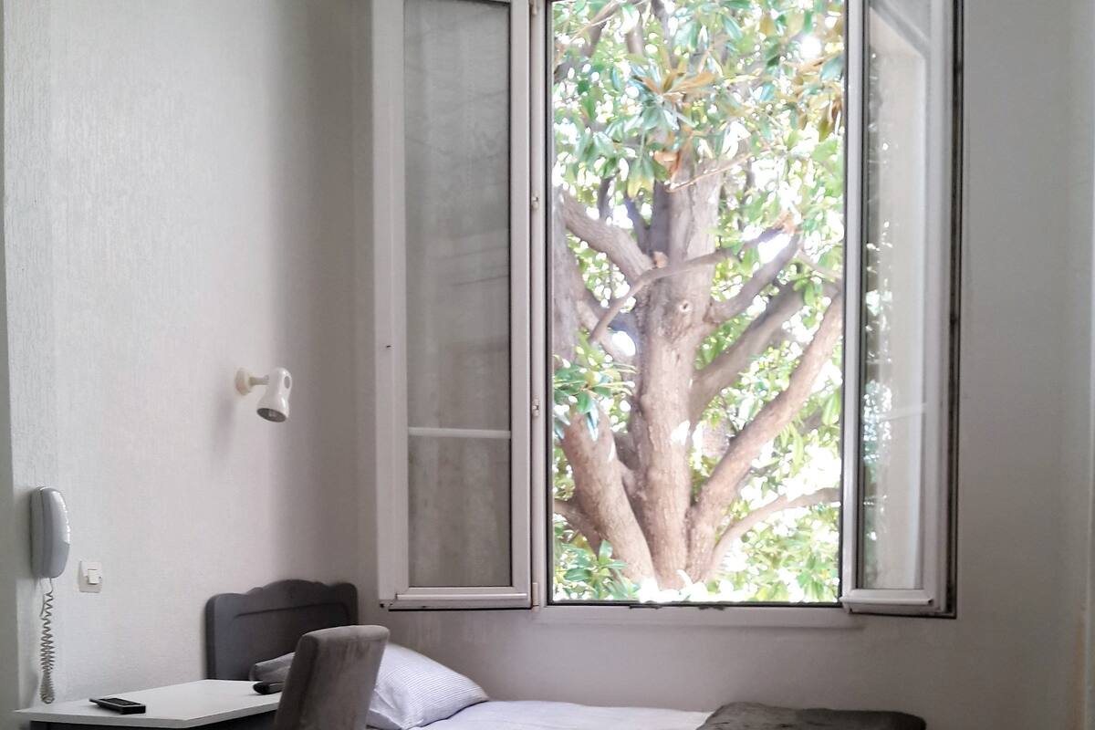 Una habitación con cama, escritorio, silla y ventana con vista a un árbol.