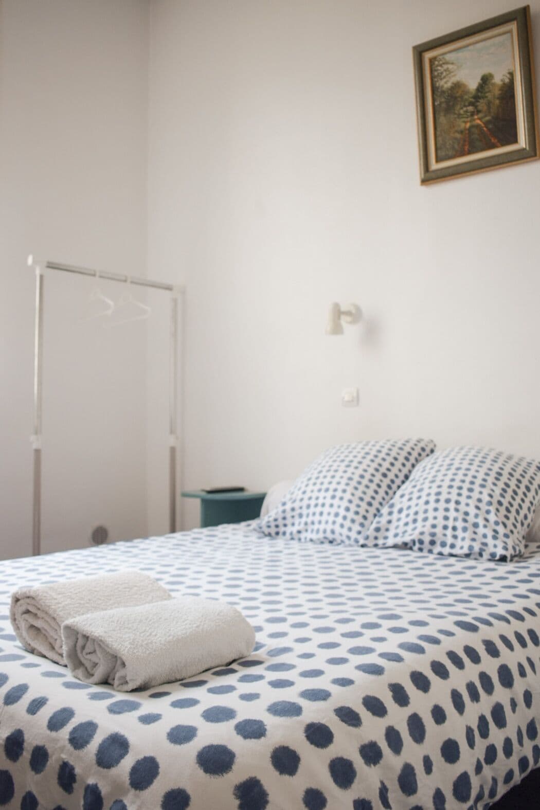A bedroom with a bed, a white towel, a painting, and a whiteboard.