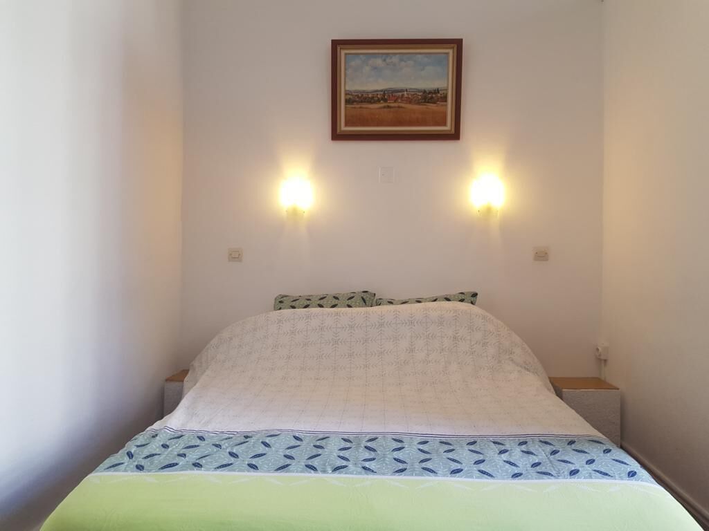 Een slaapkamer met een bed, twee wandlampen, een lijst met een afbeelding boven het bed en een nachtkastje.