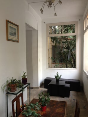 A dining area with a table, chairs, and potted plants. There is a window with a view of greenery outside. - Hôtel Belle Meunière (Nice)