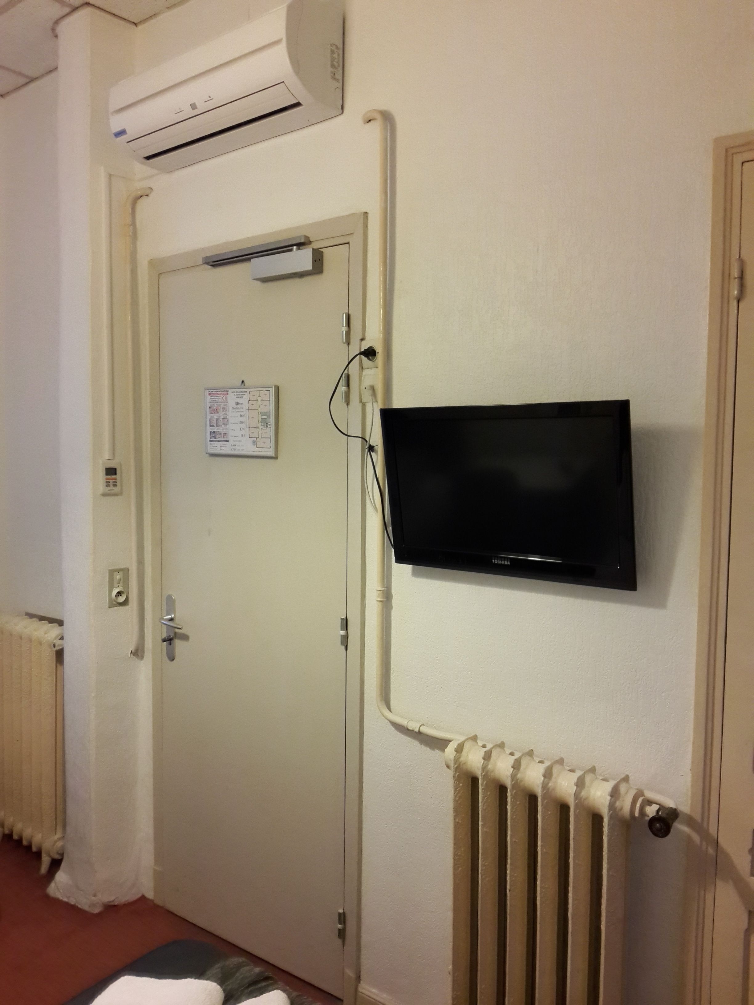 Una habitación con la puerta cerrada, un televisor montado, un equipo de aire acondicionado y un radiador.