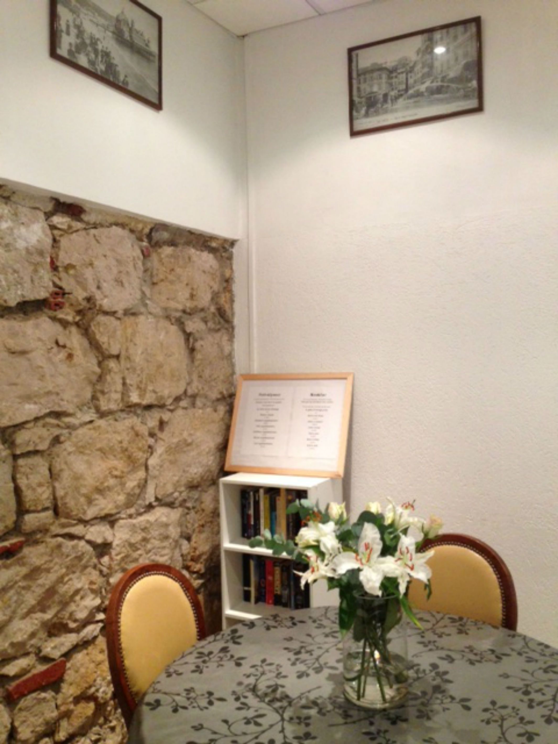 A dining area with a stone wall, a menu board, a bookshelf, and a table with a floral tablecloth.