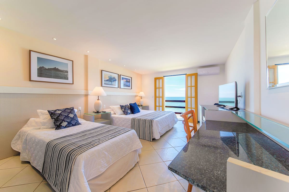 A hotel room with two beds, a desk, a chair, and a large window.