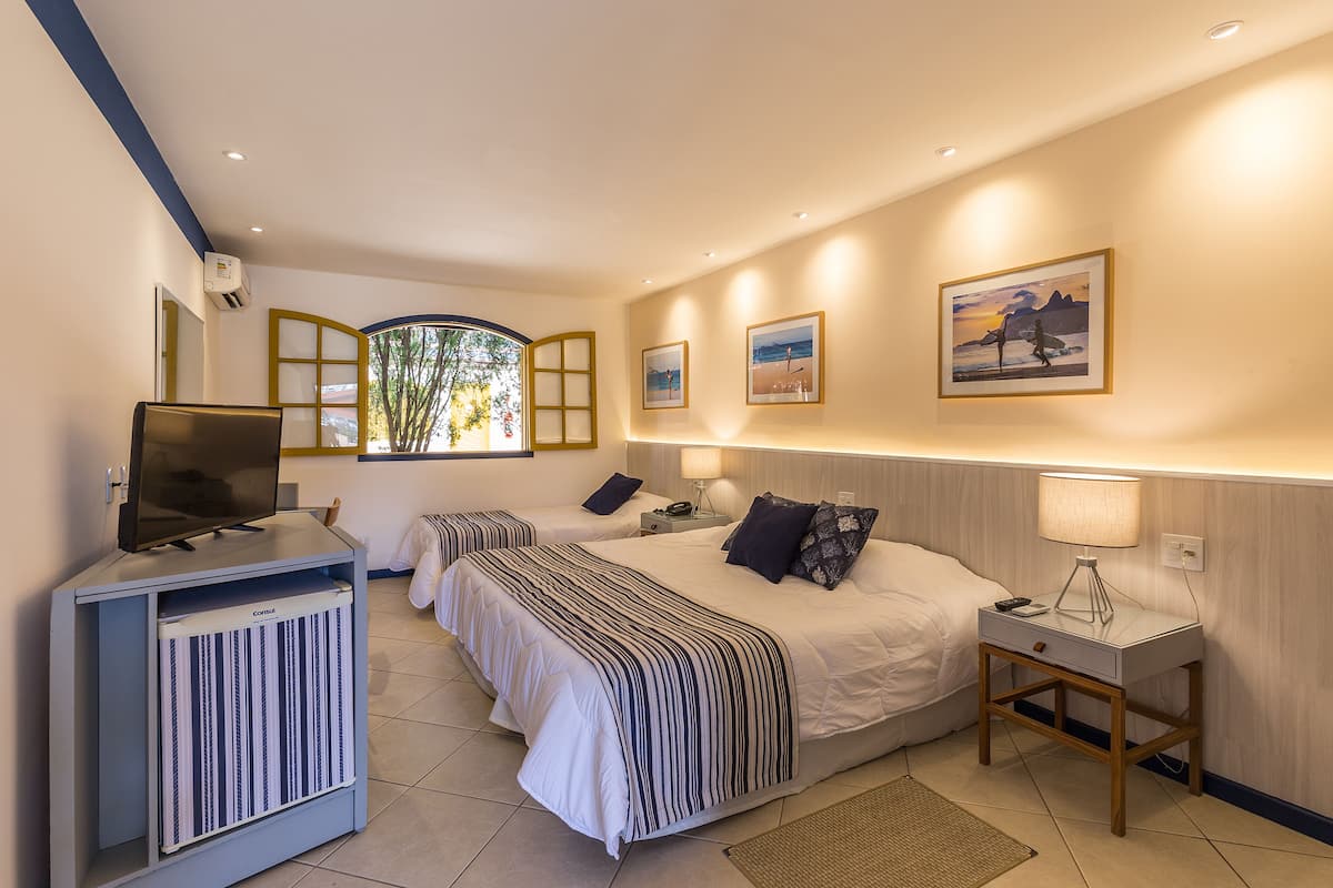 A hotel room with two beds, a TV, bedside tables, and framed pictures on the wall.