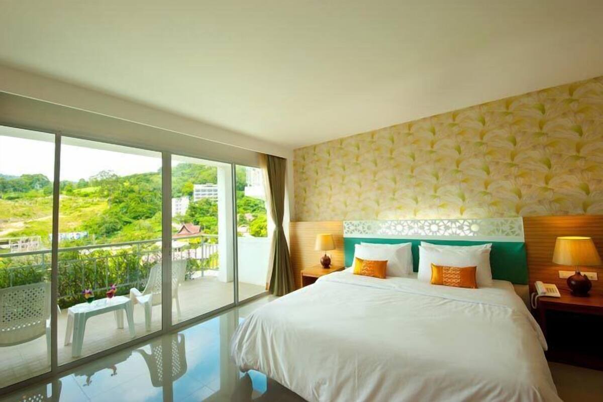 Habitación de hotel con un balcón grande, una cama con ropa de cama blanca y vistas a zonas verdes.