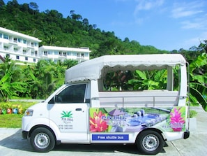 A white shuttle bus with "P.S. Hill Resort" branding and "Free shuttle bus" text, parked in front of a building with lush greenery. - P.S Hill Resort (Patong)