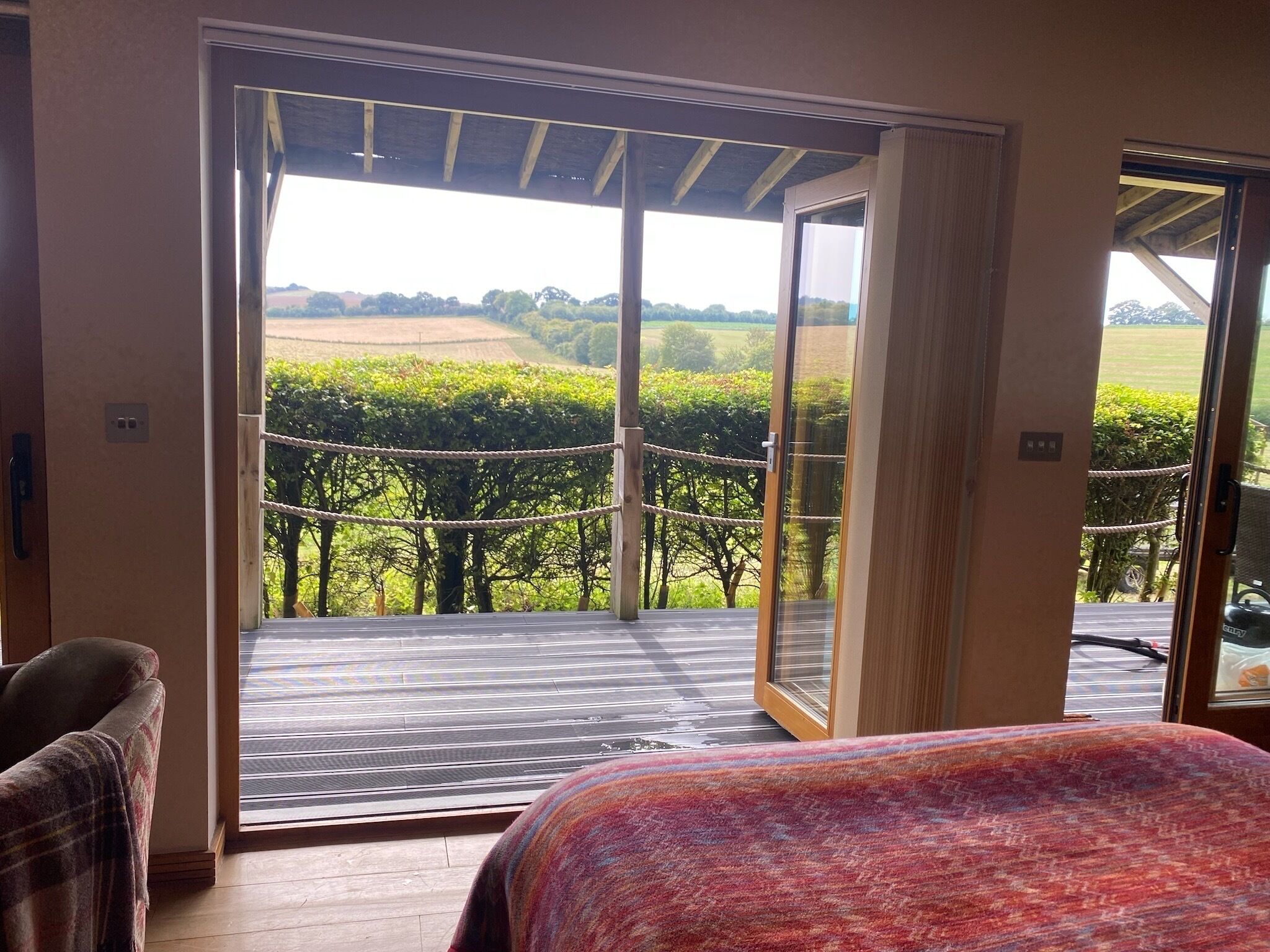 A room with a bed, a chair, and a view of a vineyard through a glass door.