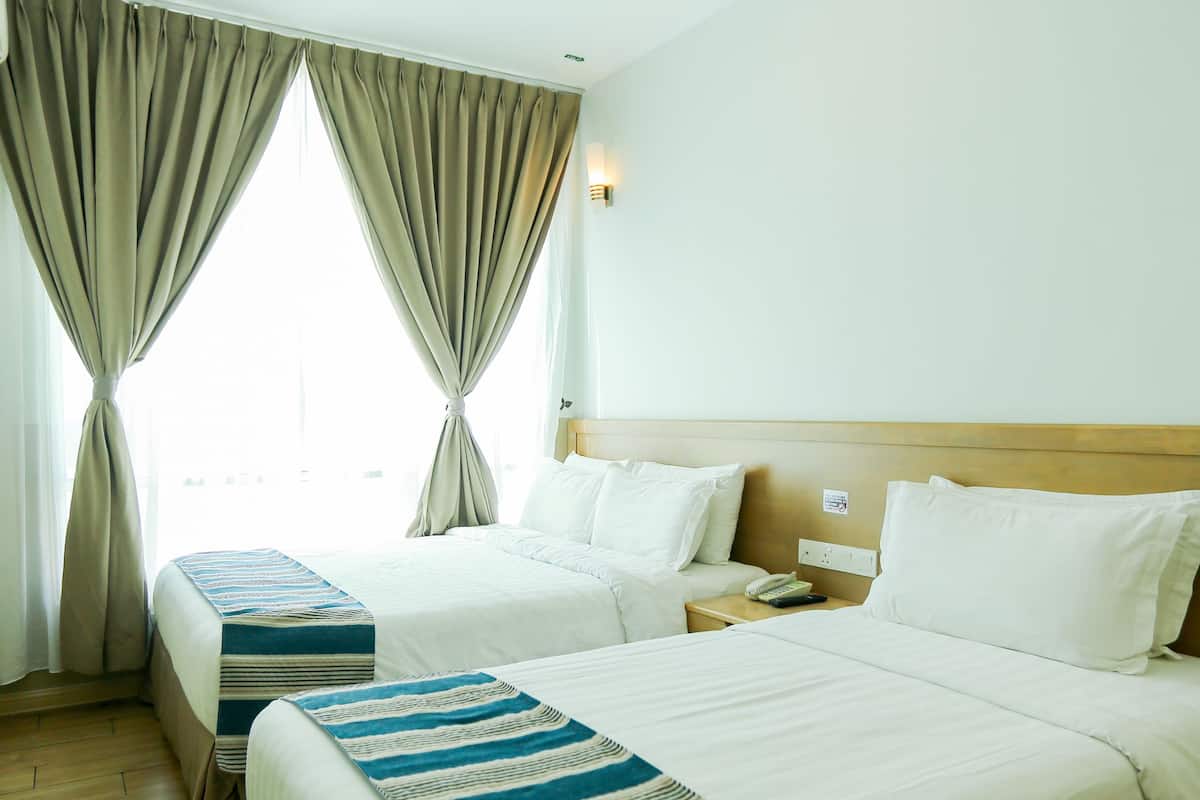 A hotel room with two beds, a wooden floor, a window with curtains, and a nightstand with a phone.