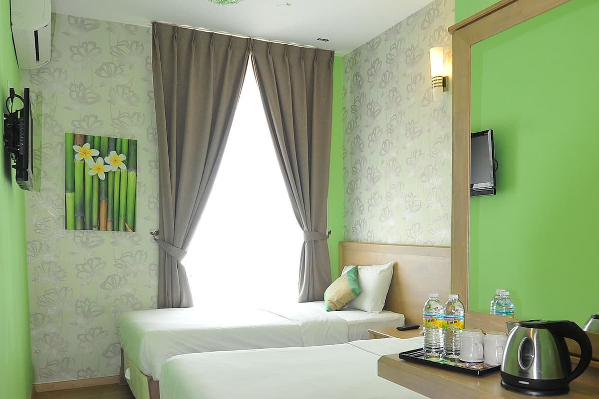 A hotel room with two beds, a wooden bench, a desk with a kettle, and a TV on the wall.