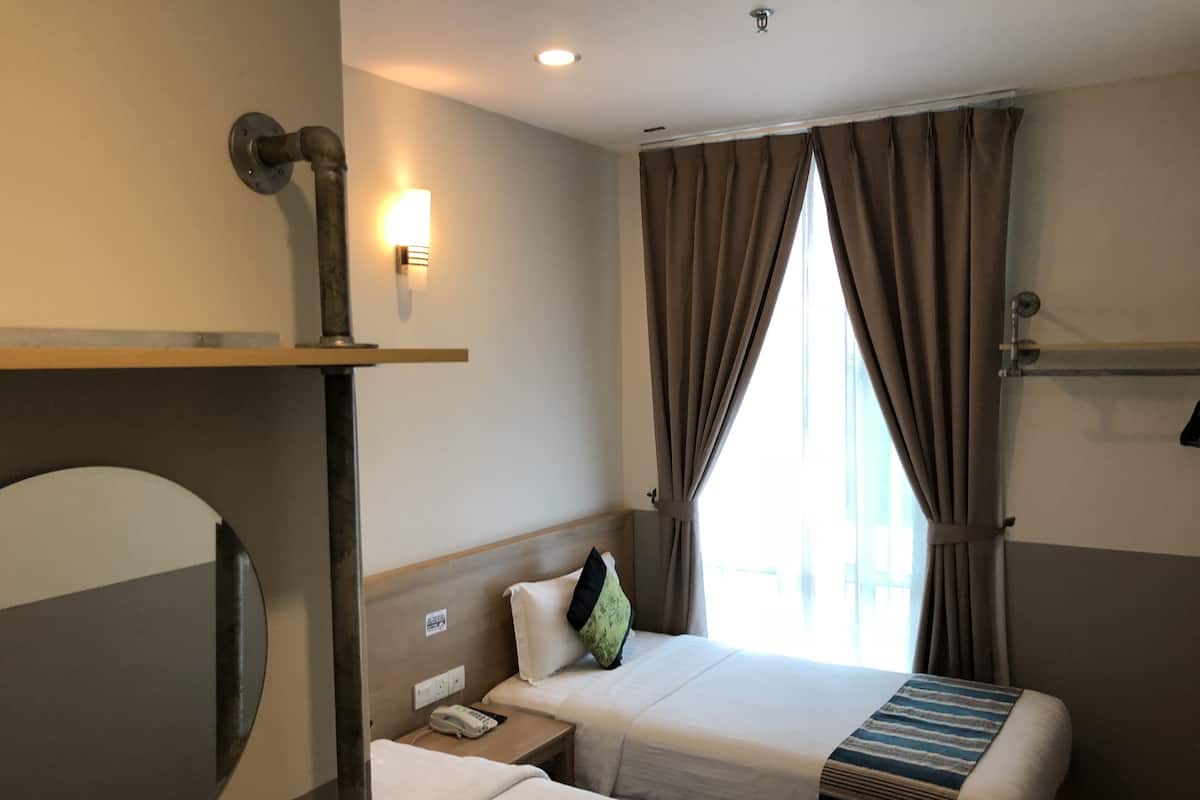 A hotel room with two beds, a bedside table with a phone, a wall-mounted light, and a window with curtains.
