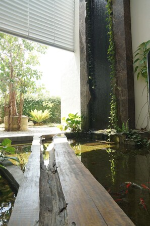 A serene indoor garden with a water feature, a wooden walkway, and various plants. - The Explorer (Malacca City)