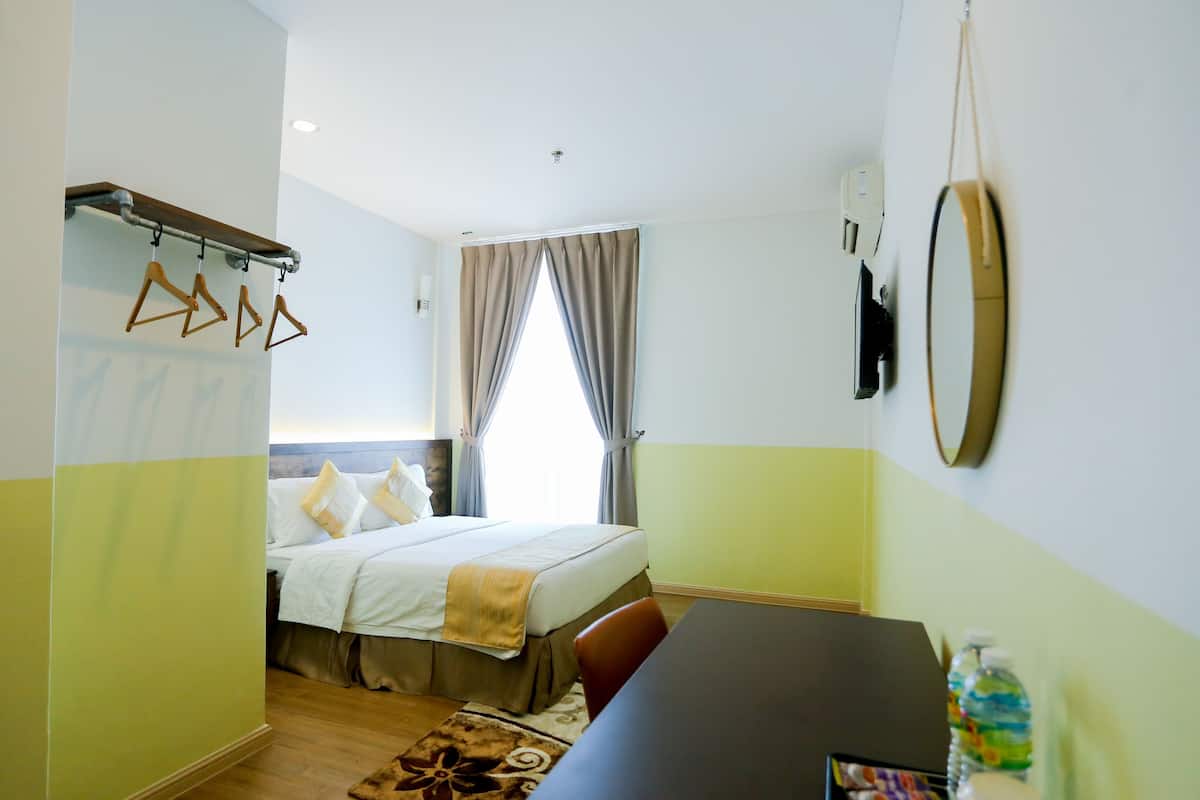 A hotel room with a bed, a desk, a mirror, and a window with curtains.