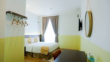 A hotel room with a bed, a desk, a mirror, and a window with curtains.