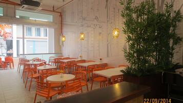 A restaurant interior with multiple tables and chairs, a large potted plant, and a wall with architectural drawings.