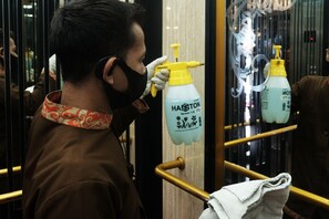 A person in a brown shirt and patterned scarf standing in an elevator, holding a spray bottle labeled "Haston". - T Series Place Serviced Apartment (Bangkok)
