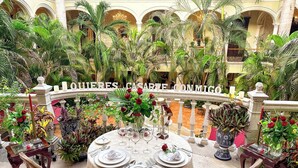 A formal outdoor dining area with a table set for four, surrounded by lush tropical plants and a decorative railing. - Mansión Merida Hotel Boutique - Restaurant  (Mérida)