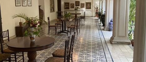 A long hallway with a patterned floor, a dining area with a round table and chairs, and a series of framed pictures on the walls.