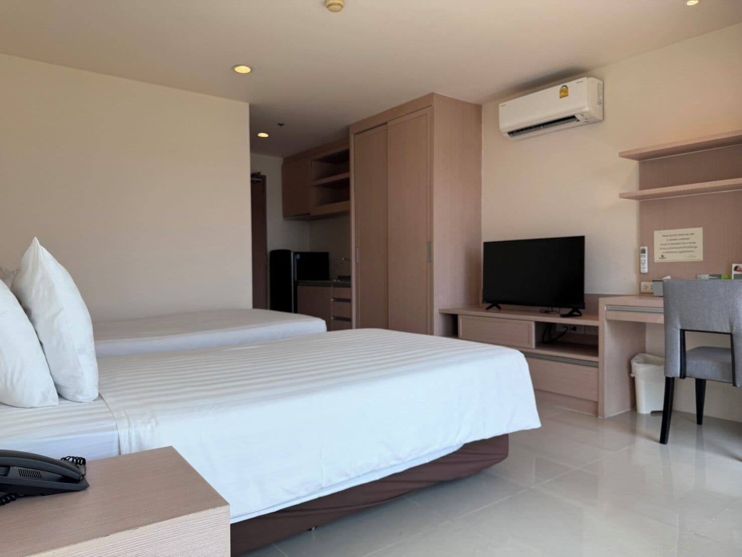 A hotel room with a bed, a desk, a television, an air conditioning unit, and a telephone.