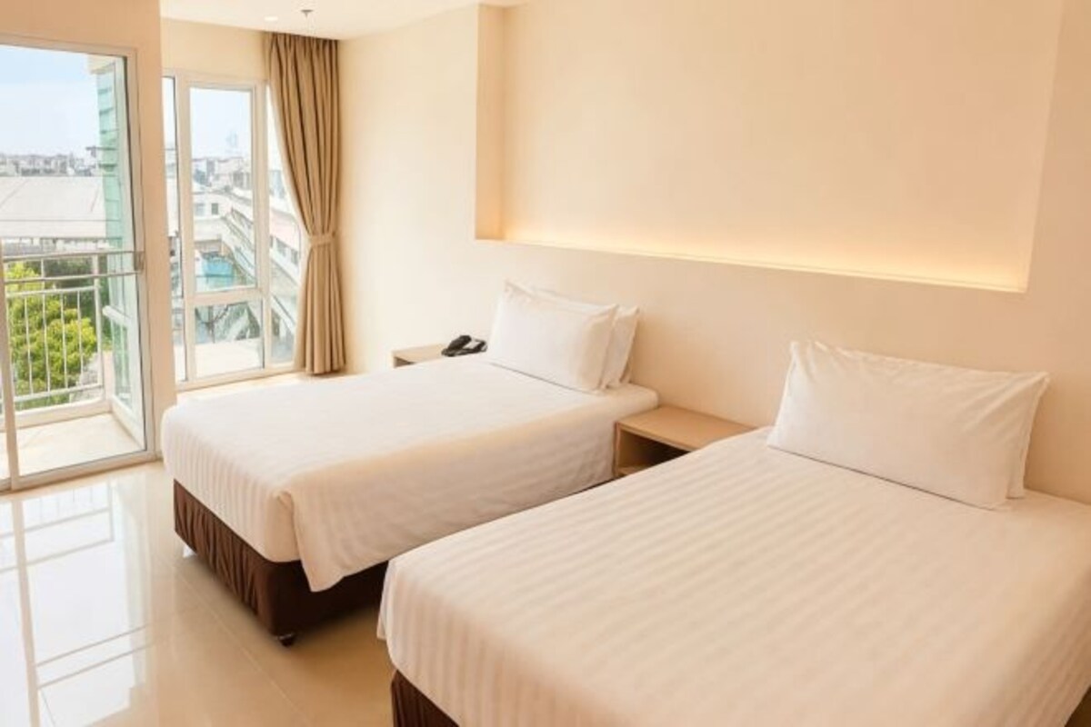A hotel room with two beds, a nightstand, a phone, and a view of the city through large windows.