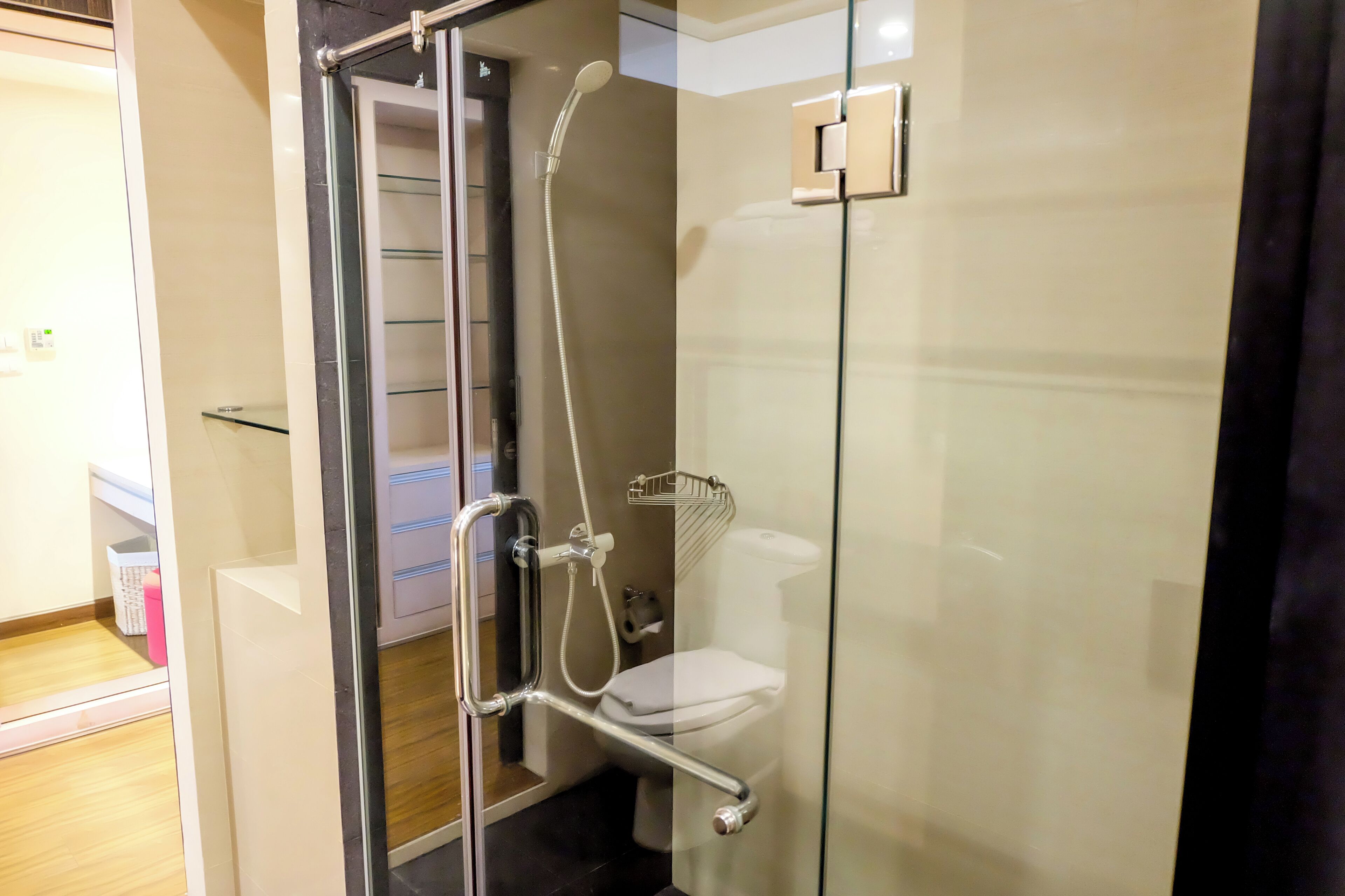 A glass-enclosed shower stall with a handheld showerhead, a glass shelf, and a toilet.