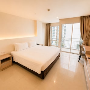 A hotel room with a large bed, a bedside table, a desk, and a view of the outside.