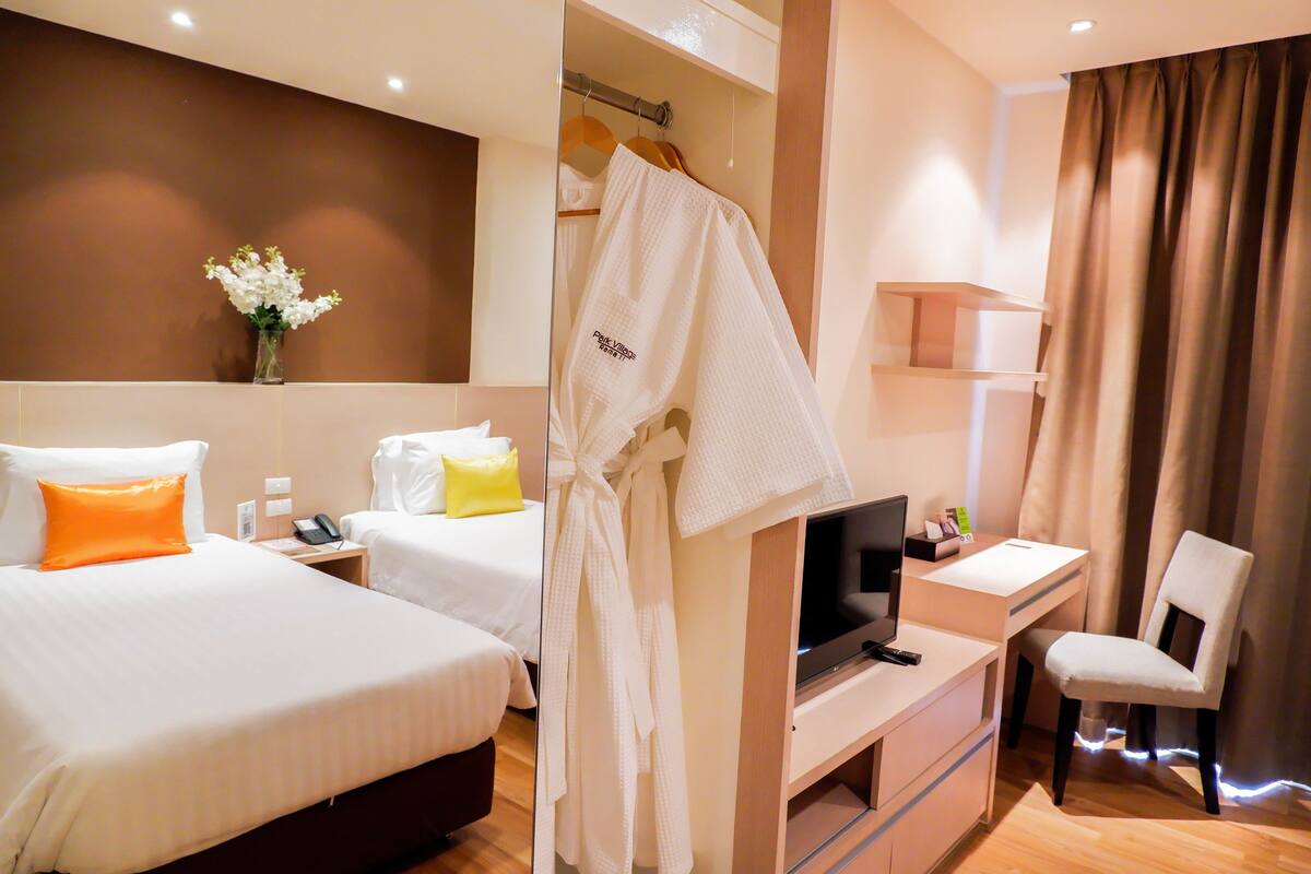 A hotel room with two beds, a desk with a TV, a chair, and a robe hanging on a rack.