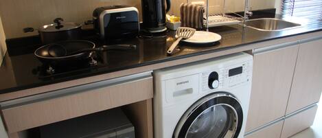 A compact kitchen with a washing machine, a microwave, a coffee maker, and a dish rack.