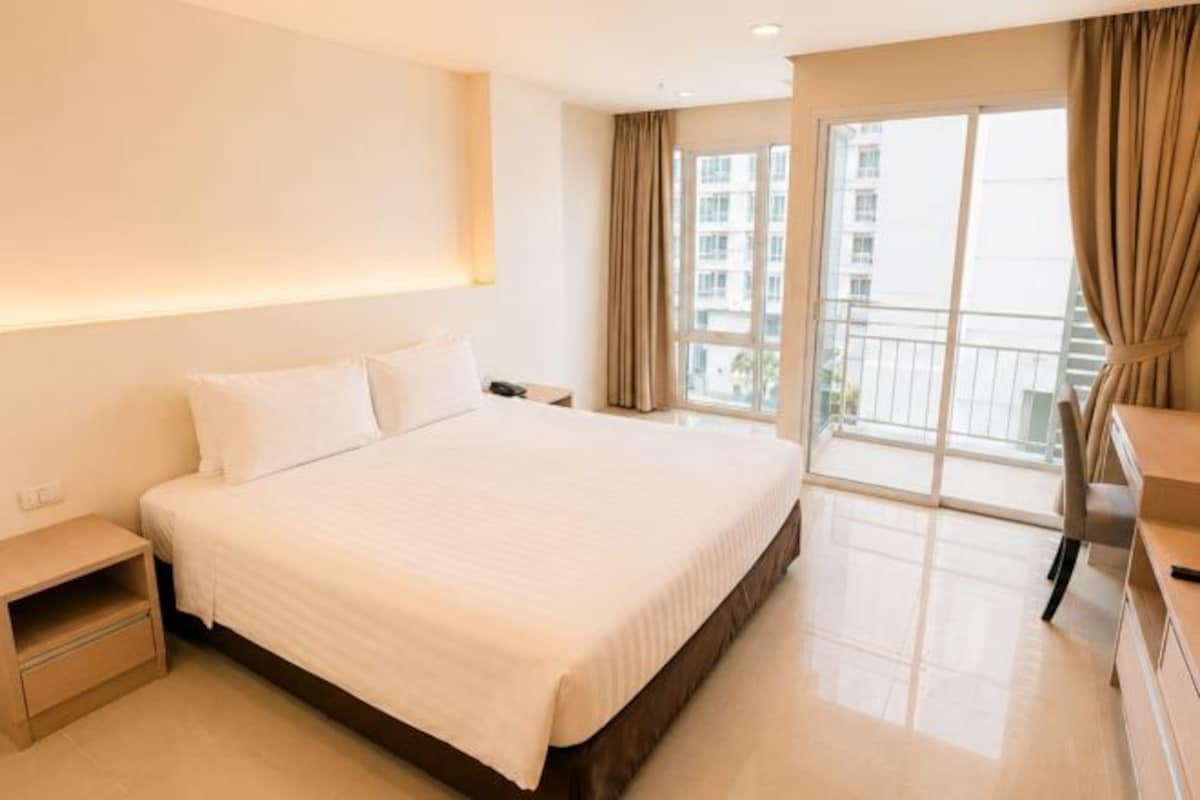 A hotel room with a large bed, bedside table, and a view of the outside.