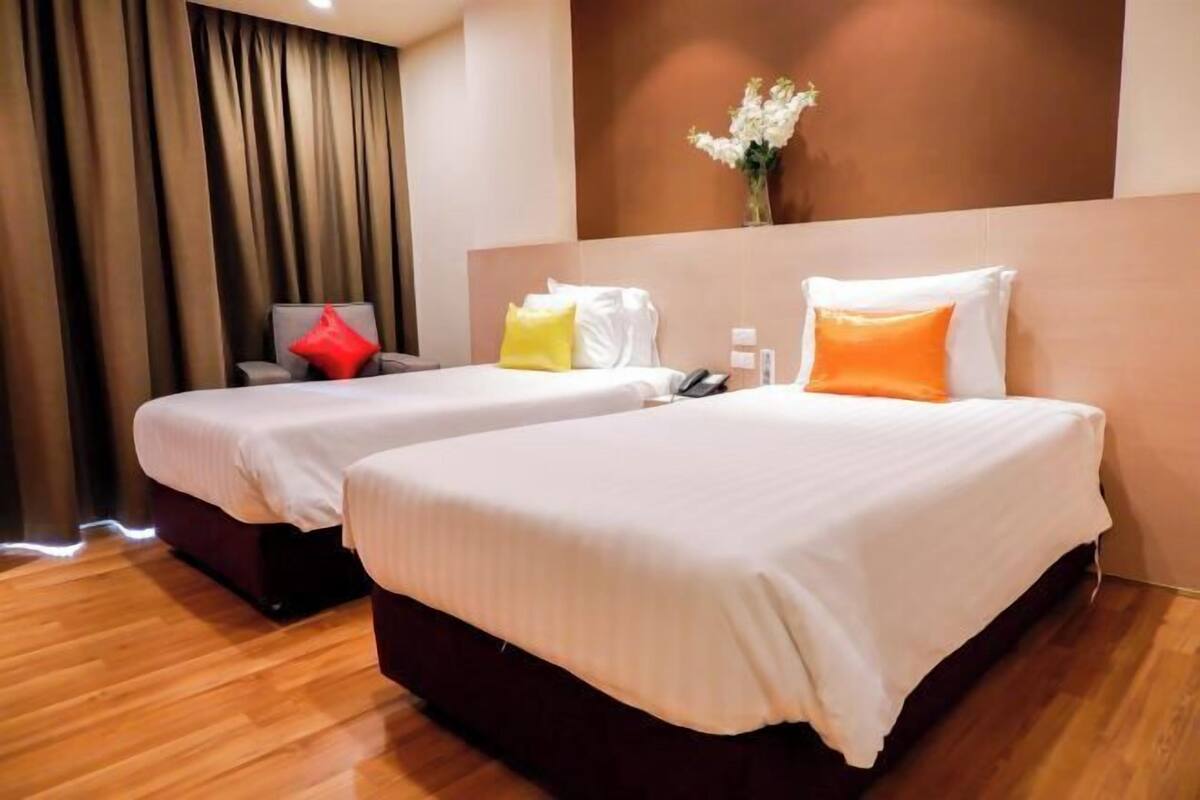 A hotel room with two beds, a chair, a vase with flowers, and a phone on the nightstand.