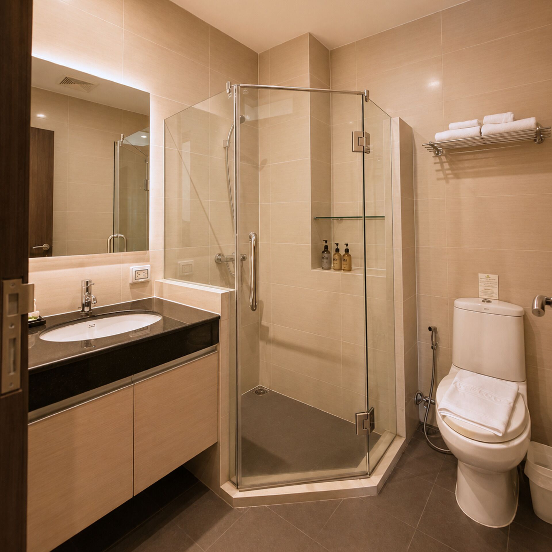 A modern bathroom with a glass-enclosed shower, a sink with a dark countertop, and a toilet with a towel rack above it.