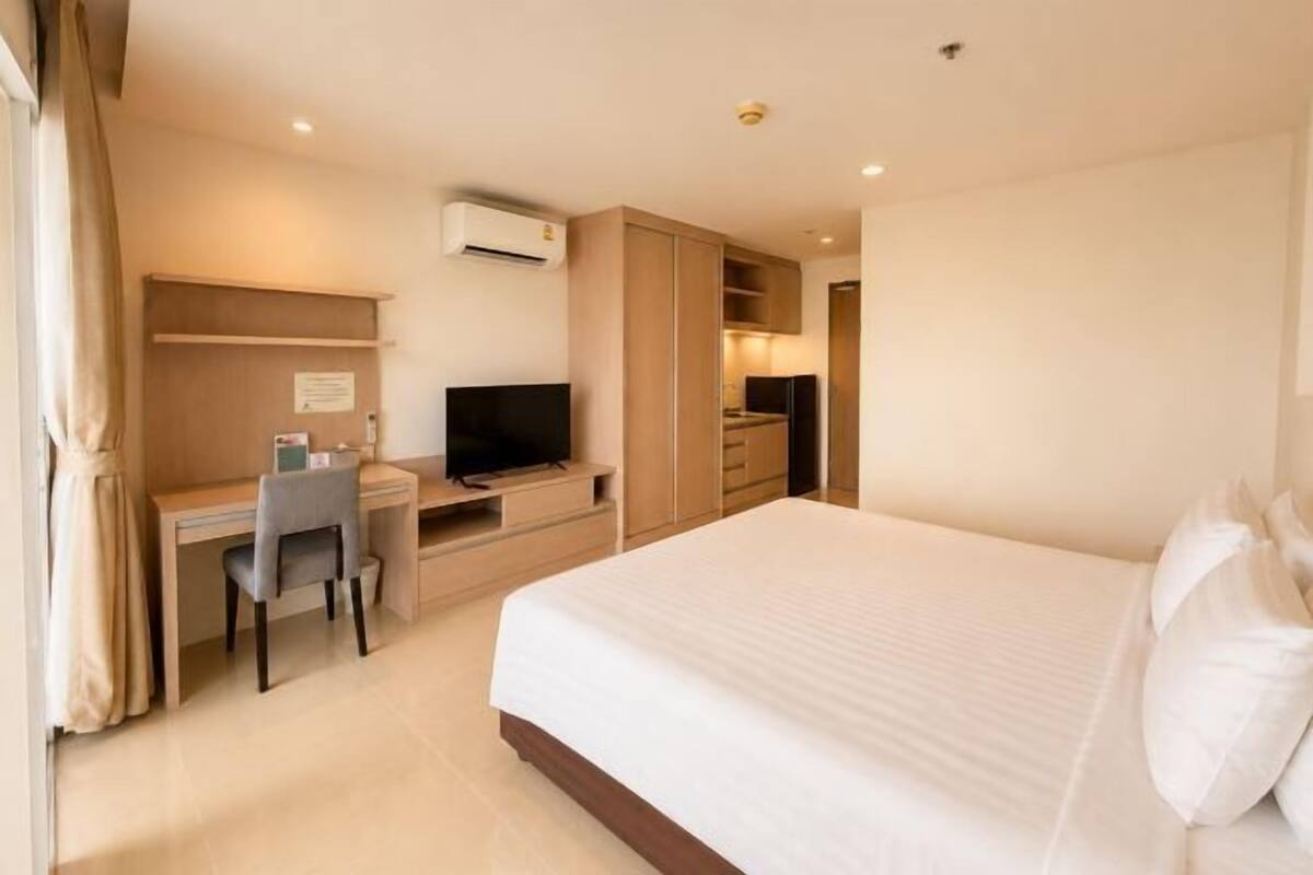 A hotel room with a bed, desk, chair, television, and a kitchenette.