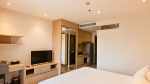 Et moderne hotelværelse med en stor seng, et skrivebord med et fladskærms-tv, et spejl og et tekøkken.