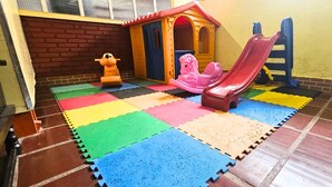 Un espace de jeux avec un toboggan, une petite maison de jeu et une girafe en jouet.