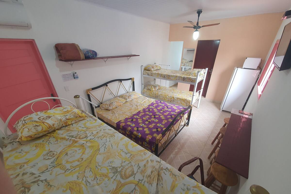 Une chambre avec deux lits, un bureau, une chaise, un ventilateur de plafond et une porte rouge.