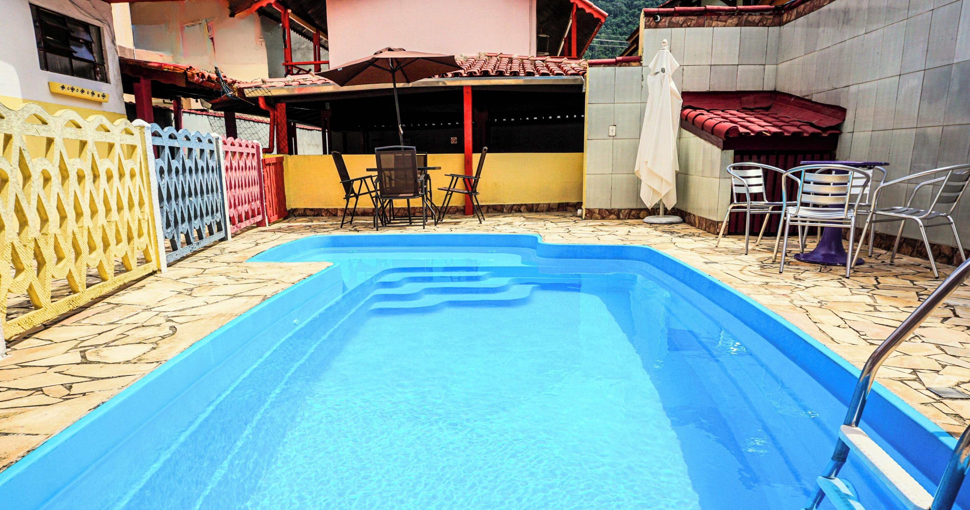 Une piscine dotée d’une terrasse carrelée, entourée d’une clôture et de chaises.
