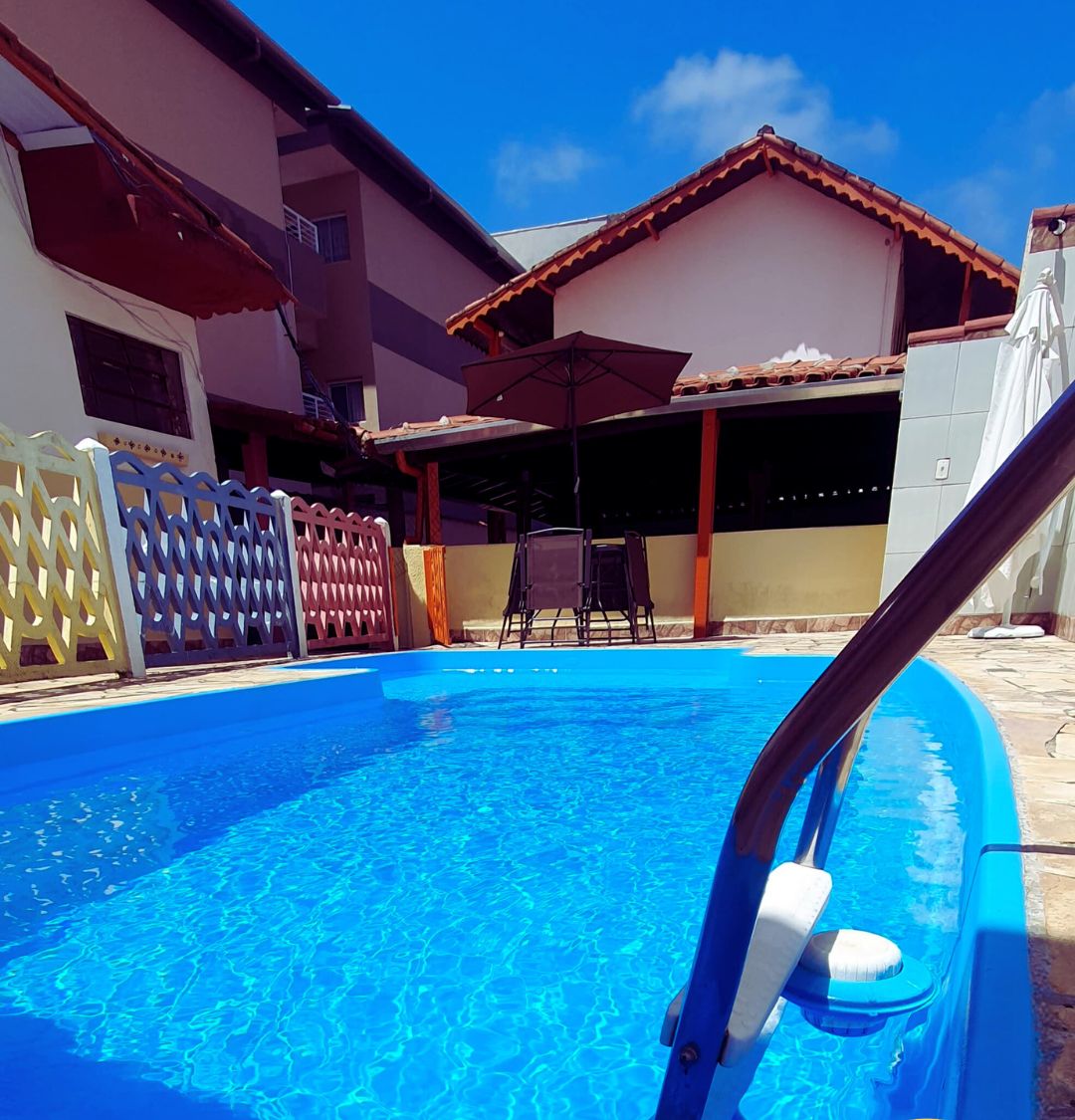 Una piscina con superficie de agua azul, rodeada por una cerca y un edificio con tejado de azulejos.