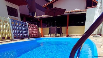 Una piscina con superficie de agua azul, rodeada por una cerca y un edificio con tejado de azulejos.