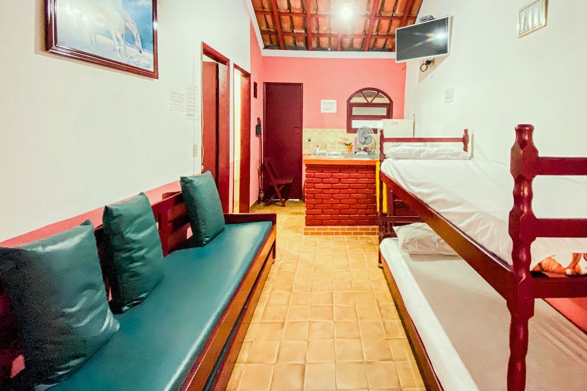Una habitación con cama, una banca, un televisor y una mesita.