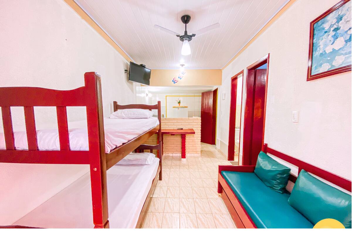 Une pièce avec des lits superposés, une petite table, un canapé et un ventilateur de plafond.